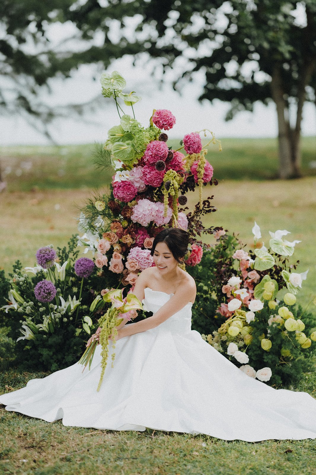 Bride seated in structured wedding gown Selene beside pink and purple garden floral installation